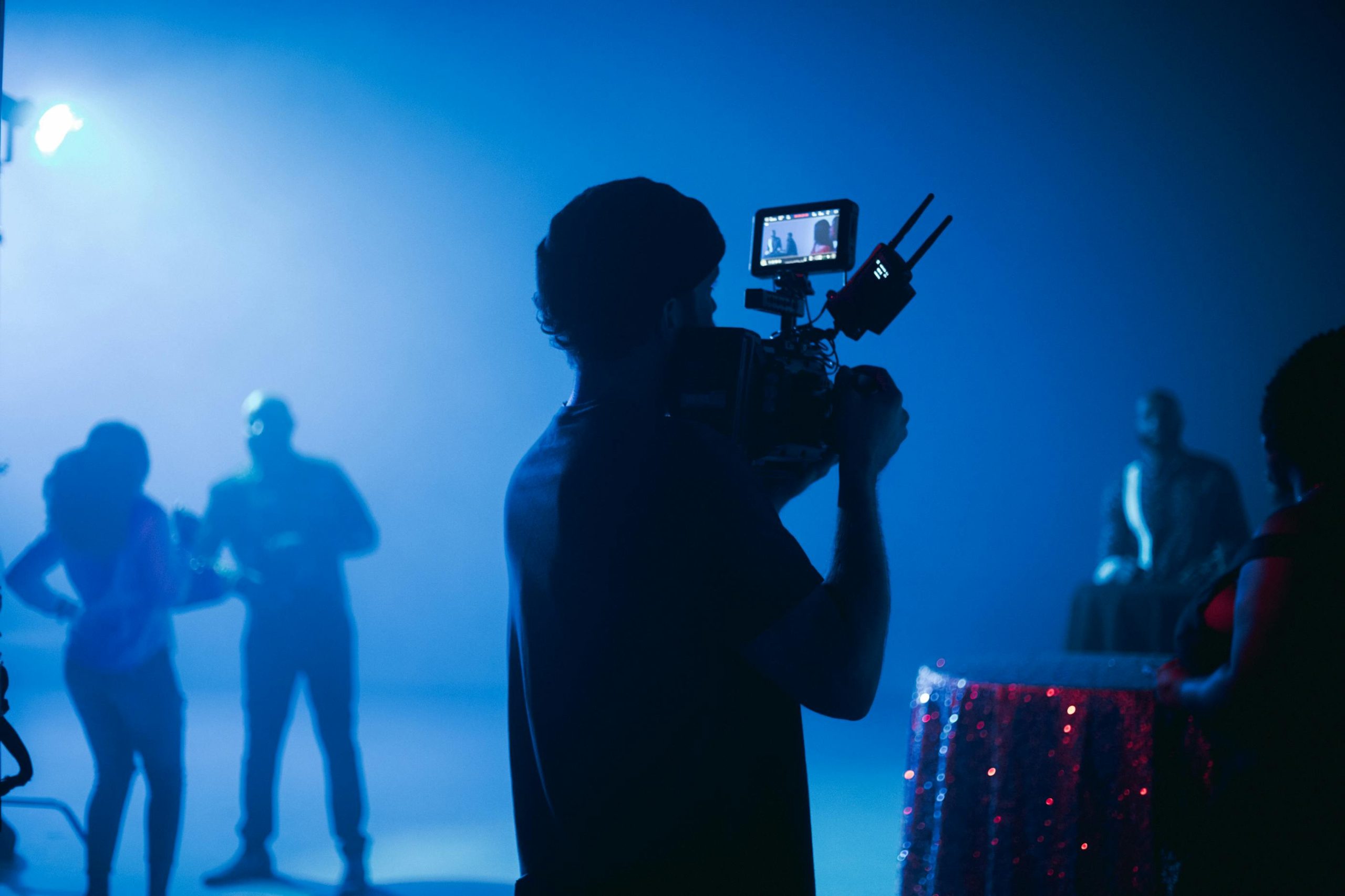 Behind-the-scenes image of a film crew and actors in a cinematic setting with dramatic lighting.